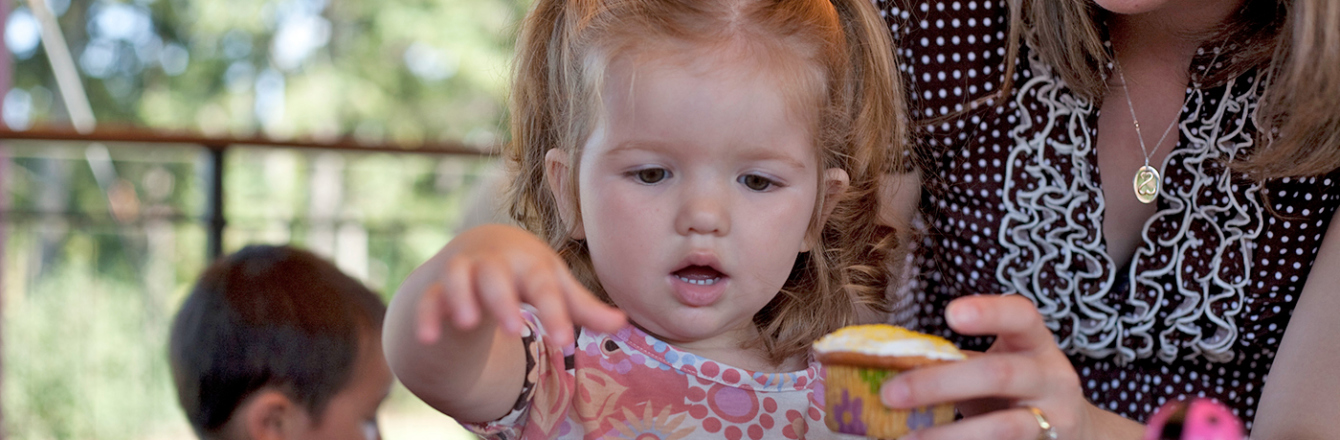 Child reaches for a cupcake at her birthday party