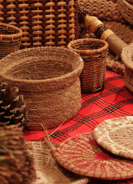 Woven pine needle baskets of varying size and shape displayed on a red tartan cloth.