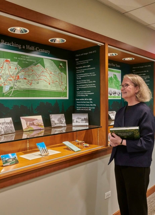 Photo of Rita Hassert standing in front of Imprinted a library display at The Morton Arboretum