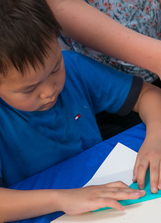 A young boy folding a piece of blue origami paper.