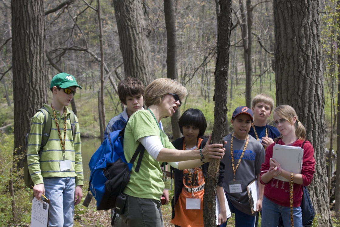 Students looking at a tree with teacher in spring