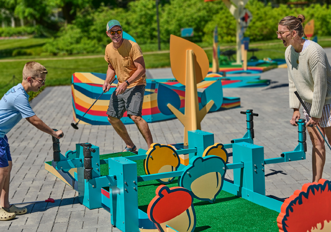 A family smiling and having a great time playing a round of Wonder Woods Mini Golf